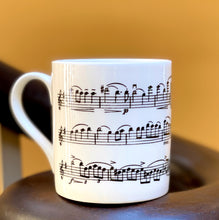 Load image into Gallery viewer, Music gift ideal for classical music fans. Elegant bone china mug with a section of Mendelssohn's Violin Concerto printed on in black. This fabulous mug is perfect for any violin player or music lover. A combination of a full capacity of 310ml and a subtle lip and classic handle design makes this mug both comfortable and stylish. Microwave and dishwasher safe. Height 85mm; Diameter 77mm. View from left 2 thechord.co.uk